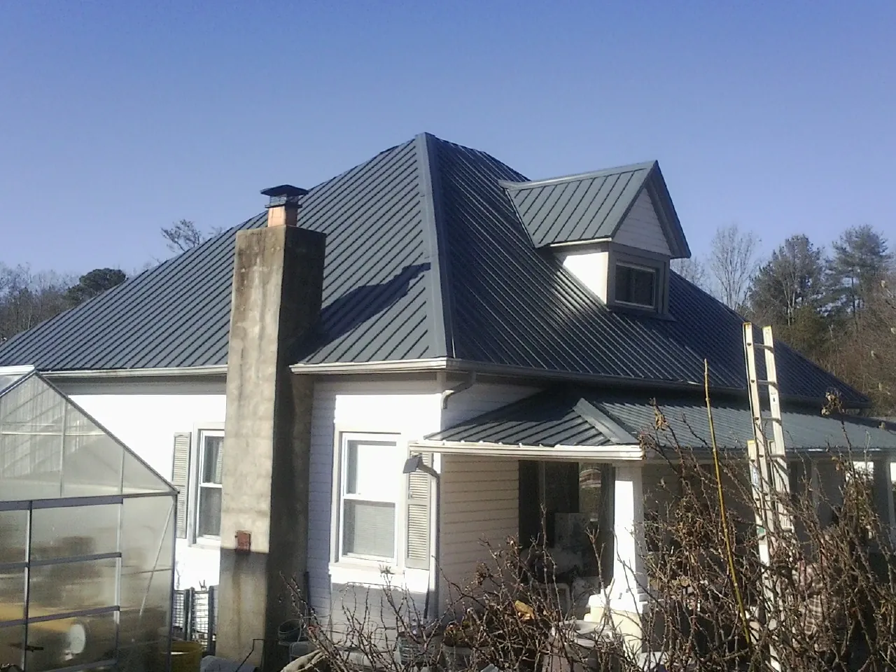 Dark blue standing seam metal roof on a white farmhouse with dormer — Slate & Tile Roof Repair by Roofing Brothers in Scipio
