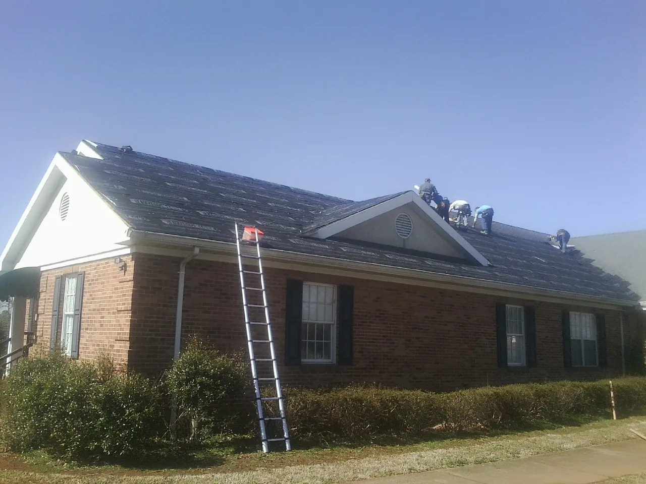 Crew tearing shingles off a brick ranch roof with a ladder set — Emergency Roof Repair work by our crew in Scipio