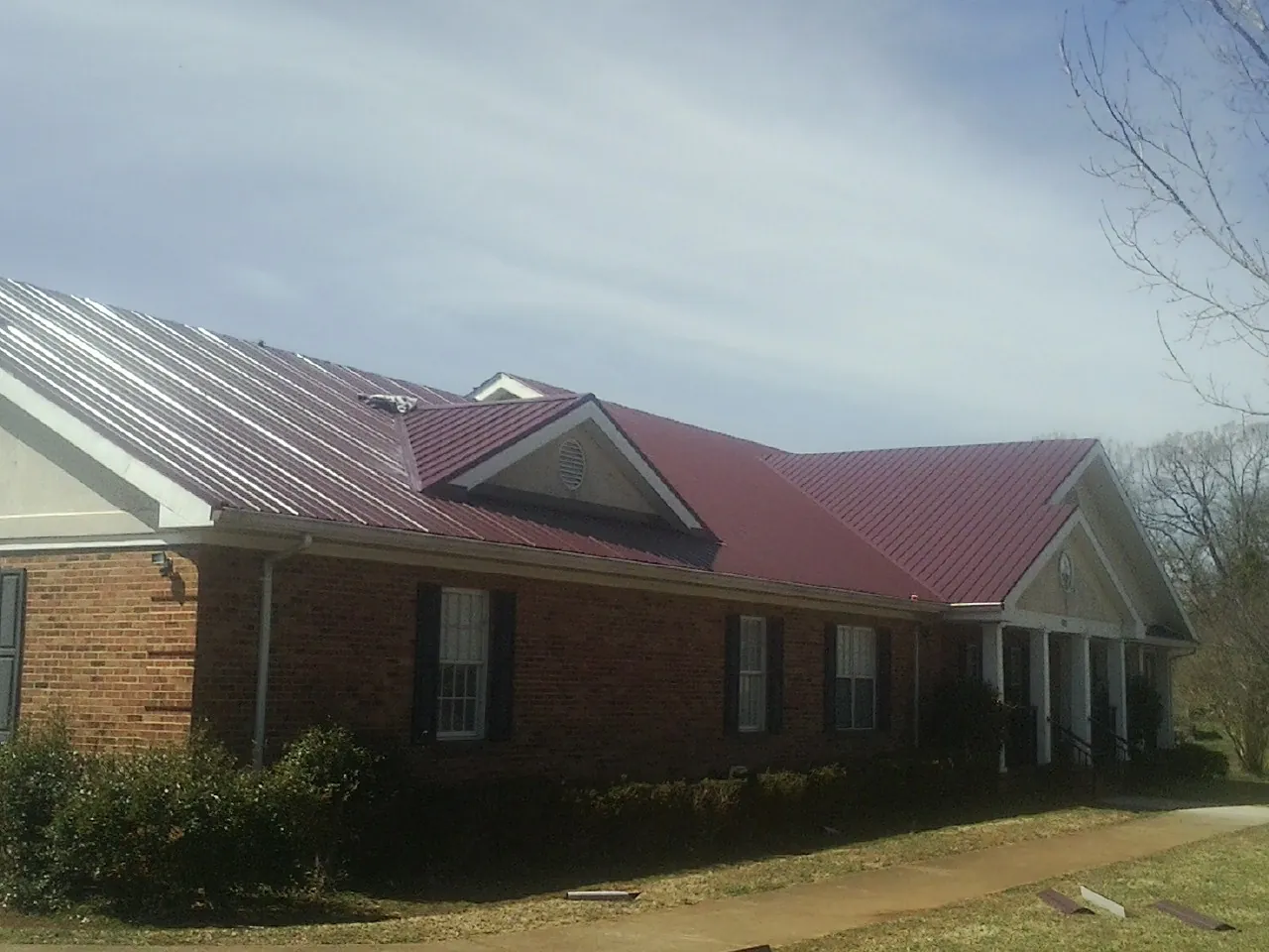 Red metal roof with gabled entries on a long brick building, from a Hail Damage Roof Repair job in Scipio