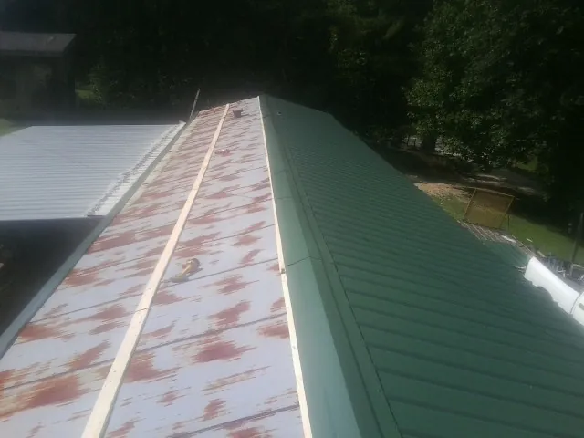 Old rusted panels beside newly installed green metal roofing — Wind Damage Roof Repair by Roofing Brothers in Scipio