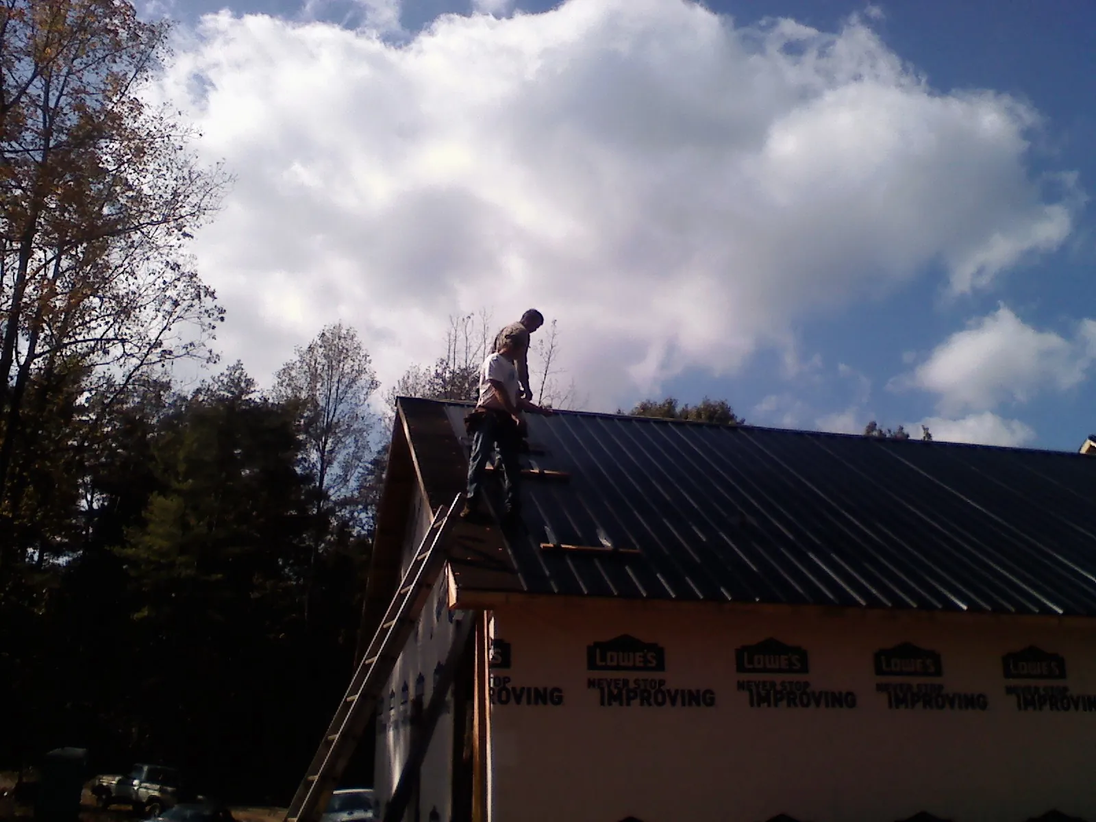 Roofer fastening dark metal panels high against a cloudy sky, from a Roof Inspection job in Scipio