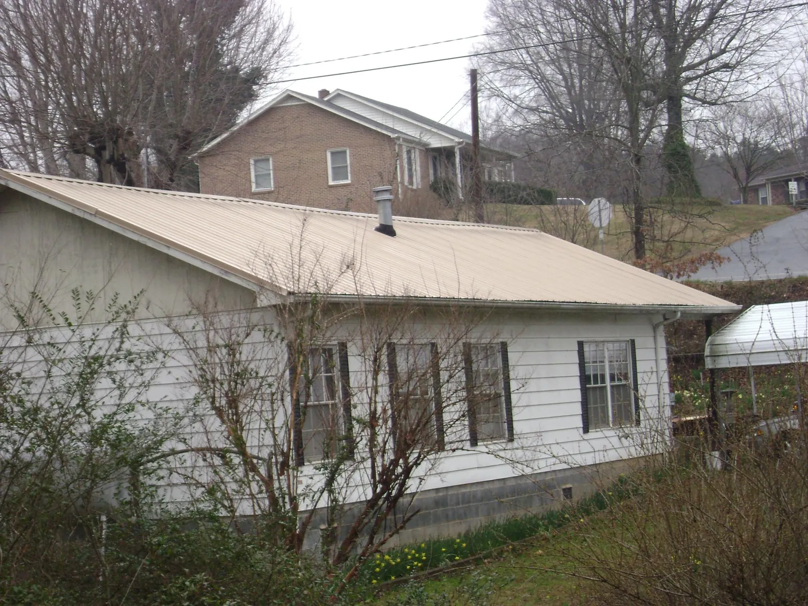 Tan metal roof on a white sided house set into a hillside — Commercial Roofing by Roofing Brothers in Scipio