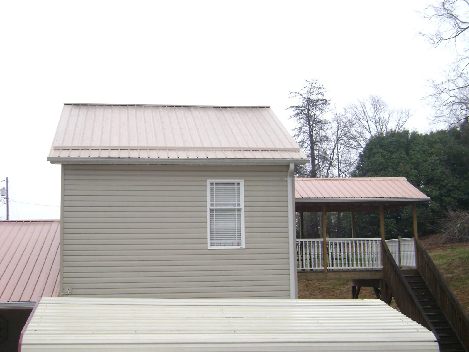 Tan metal roofs on a two story addition and attached porch, from a Roof Replacement job in Scipio